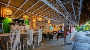 A bar area with wooden chairs, a counter with bottles, and a thatched roof. - Naturale Villa (Lembongan Island)