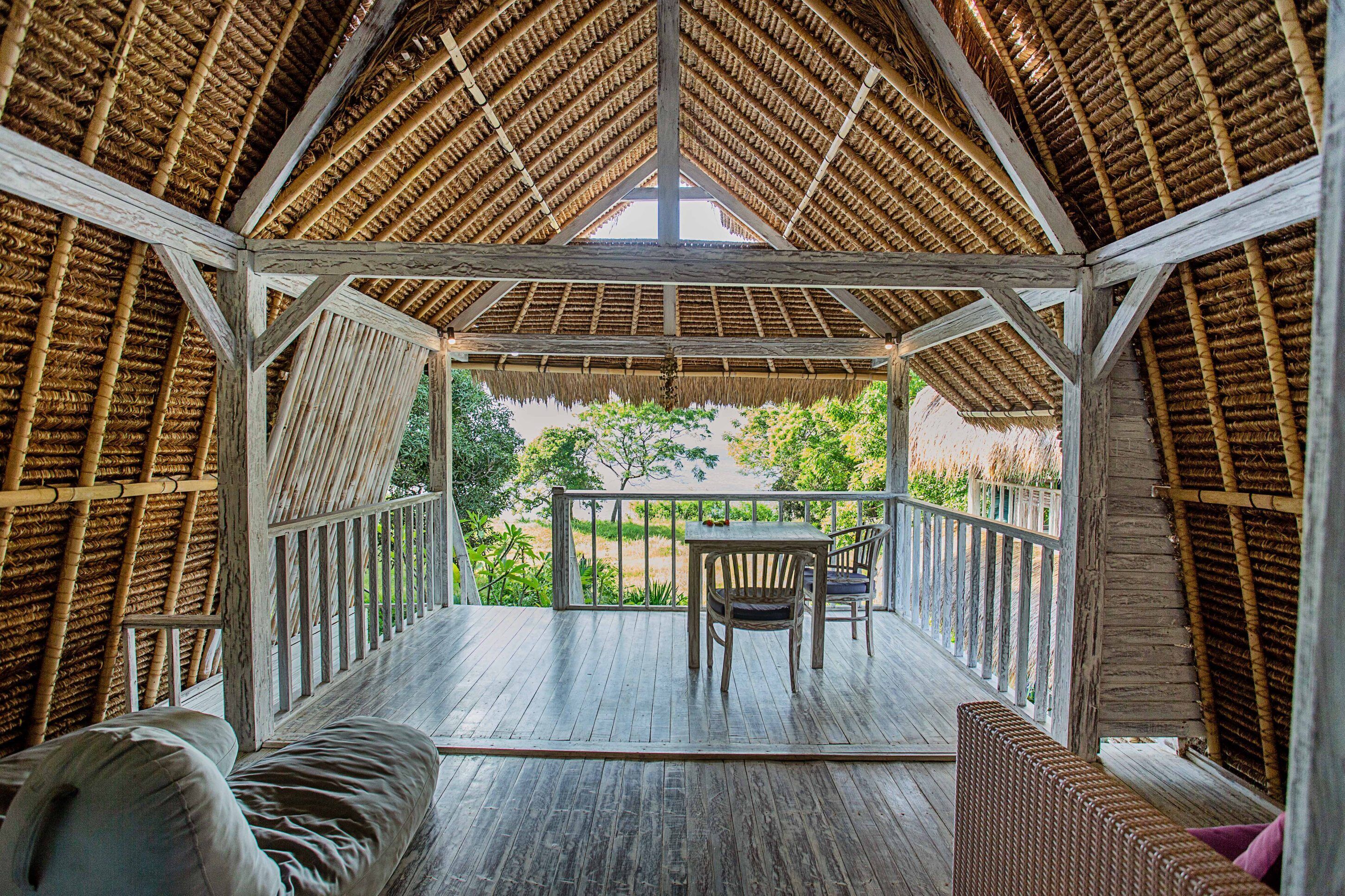 Un espace extérieur abrité, doté d’une table et de chaises en bois, entouré d’une balustrade en bois et offrant une vue sur la verdure.