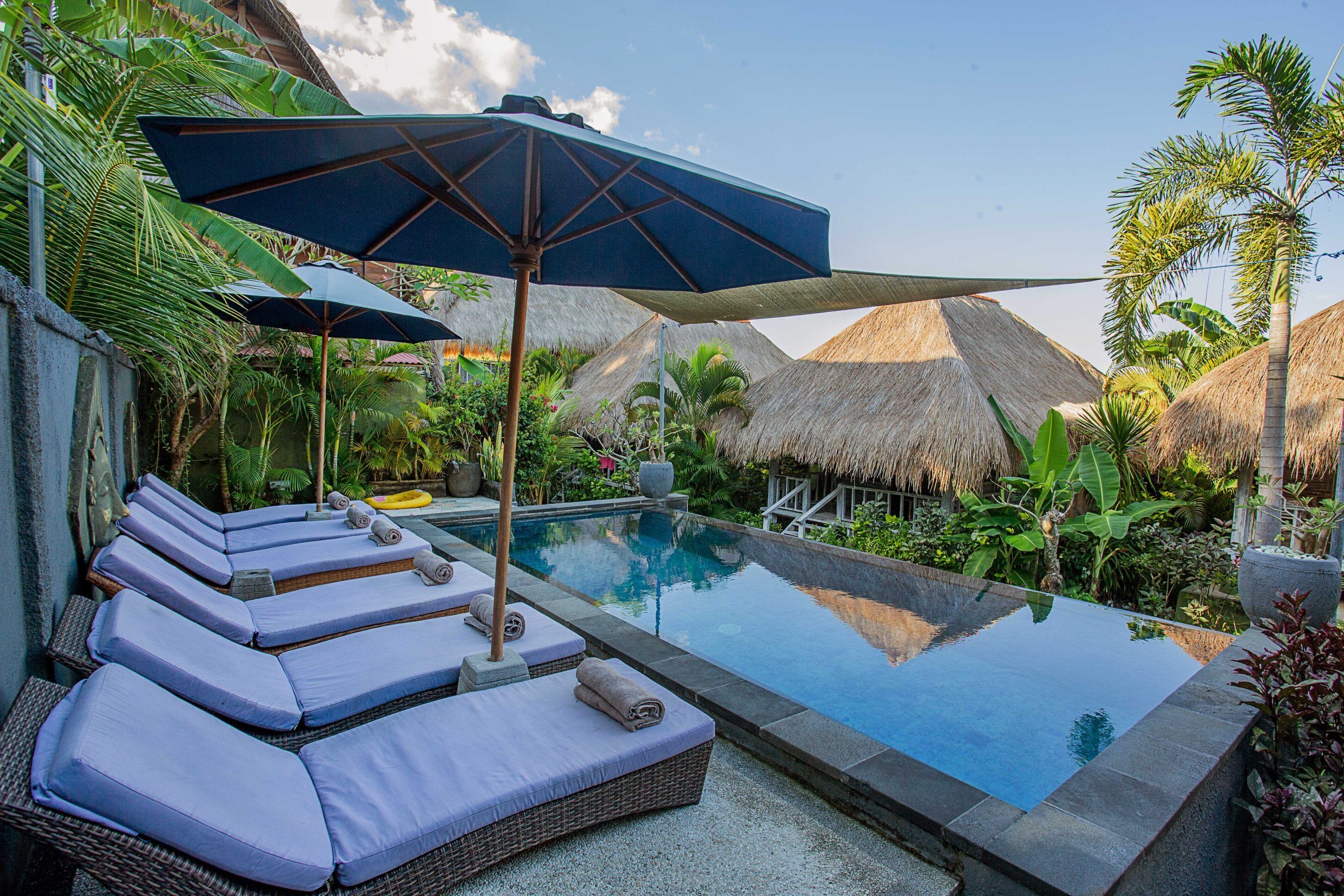 A private pool area with lounge chairs and umbrellas, surrounded by tropical plants and thatched-roof structures.