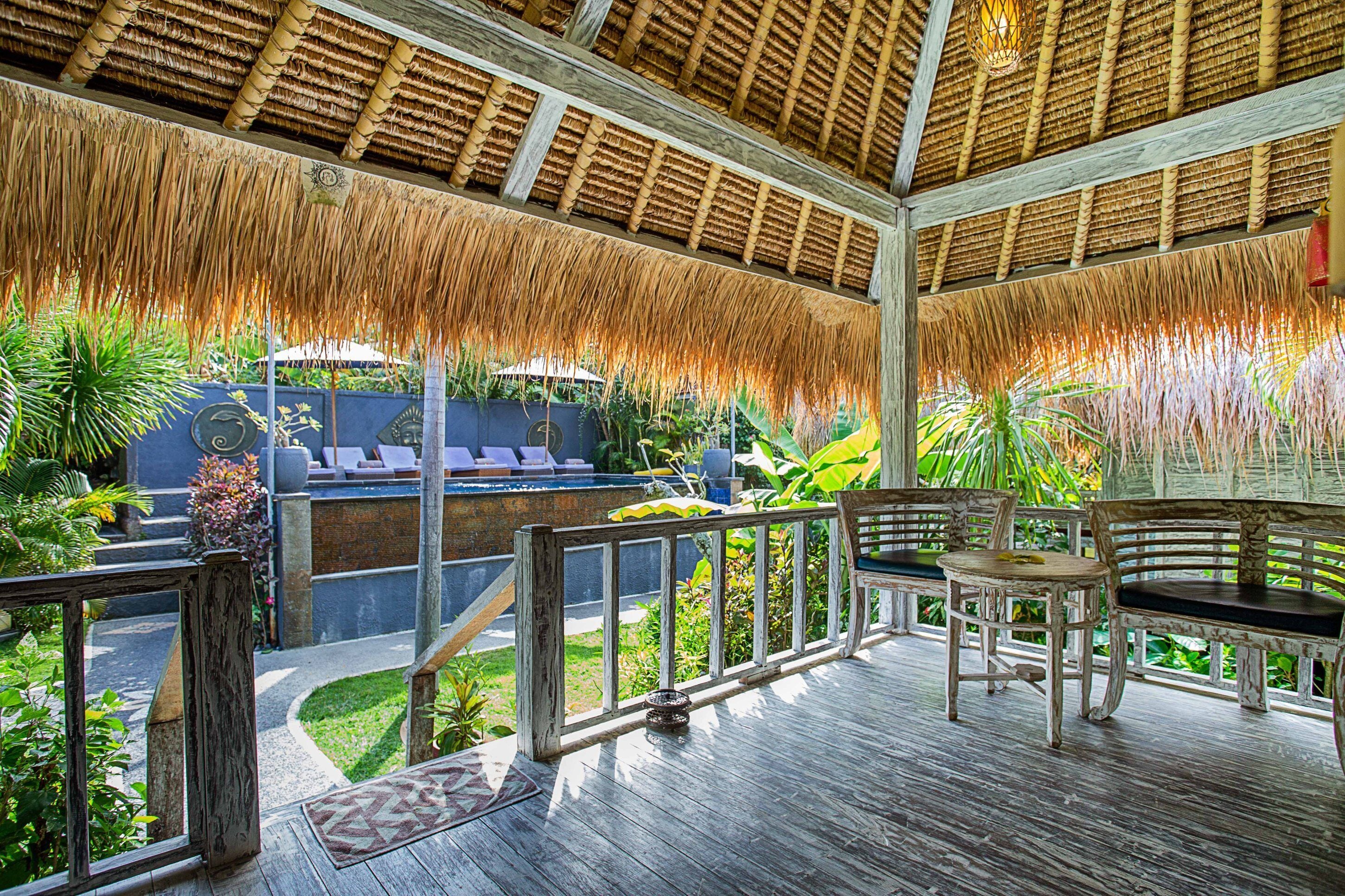 Une terrasse en bois avec un toit de chaume, des sièges d’extérieur et une végétation luxuriante.