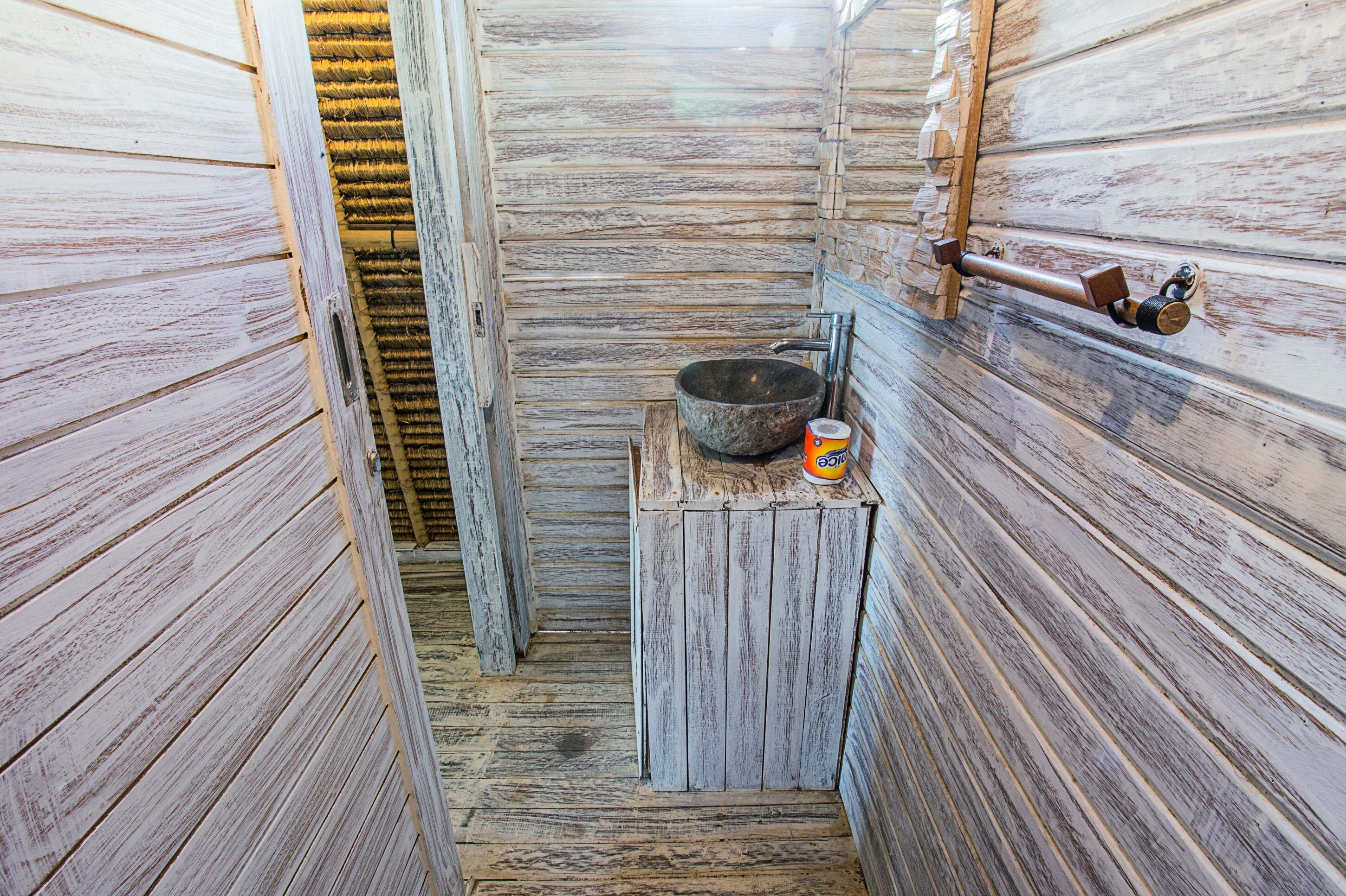 Un baño rústico y estrecho de madera, con un lavabo de piedra, un banco de madera y un dispensador de toallas.