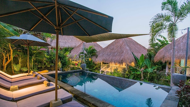 A pool area with lounge chairs and umbrellas, surrounded by thatched-roof structures and tropical plants. - Naturale Villa (Lembongan Island)