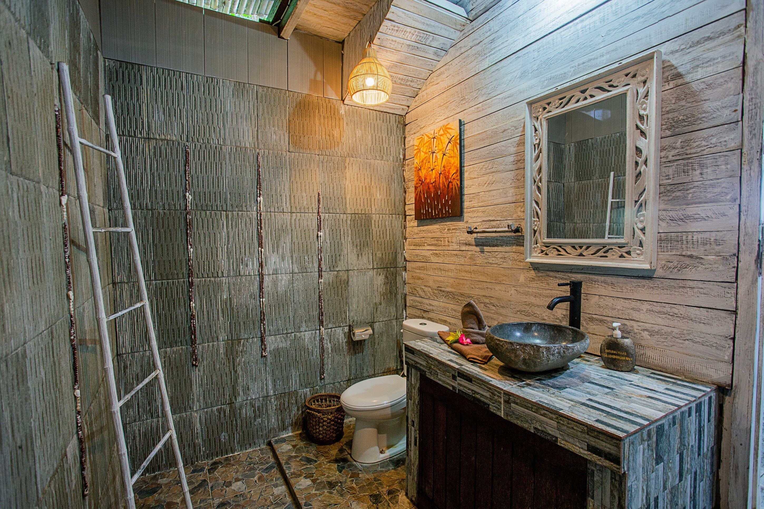 A rustic bathroom with a stone wall, a wooden vanity, a large bowl sink, and a toilet.