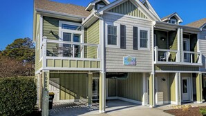 A multi-story residential building with a balcony on the second floor, a covered entryway, and a sign indicating a beach location.