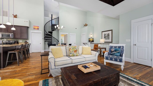 A spacious living room with a sofa, coffee table, and a dining area with chairs. A staircase leads to an upper level.