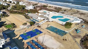 An aerial view of a coastal resort with multiple swimming pools, tennis courts, and a beach area.