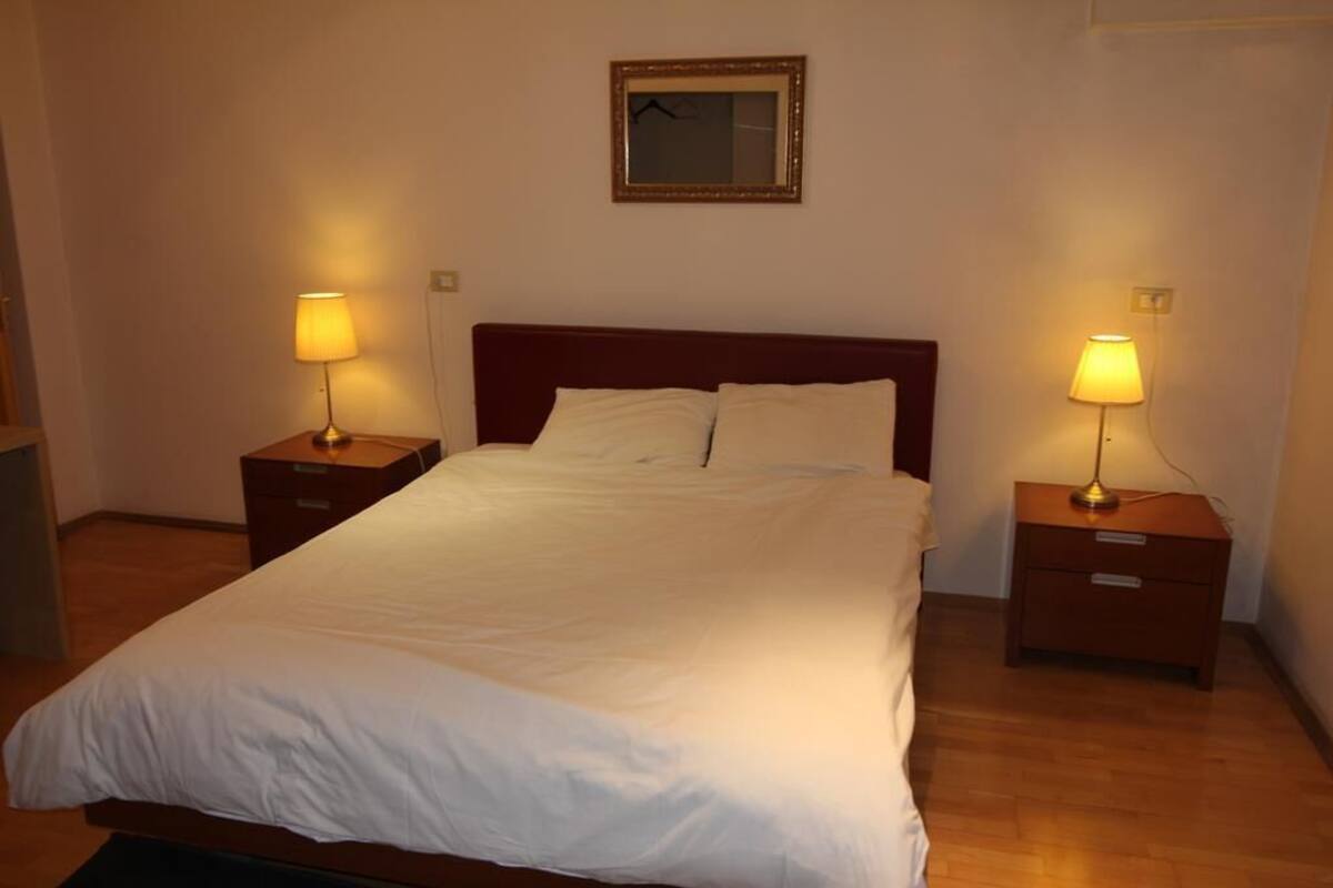 A neatly made bed with white linens, two bedside tables with lamps, and a framed mirror on the wall.