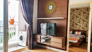 A modern living room with a flat-screen TV, wooden cabinets, a glass coffee table, and a large window with curtains.