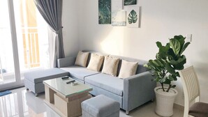 A modern living room with a grey sofa, a glass coffee table, and a potted plant.
