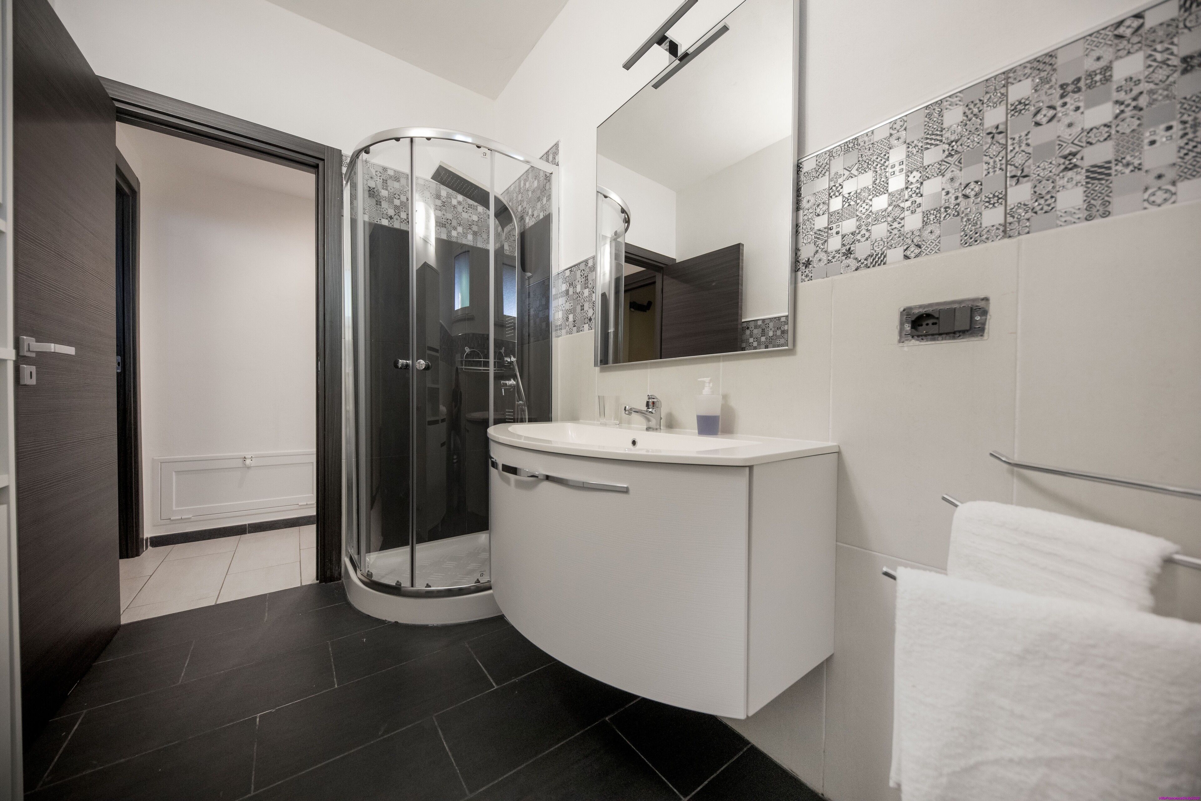 Une salle de bain moderne avec une douche à parois de verre, un meuble-lavabo blanc avec un miroir et un porte-serviettes.