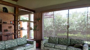 A living room with two patterned sofas, a brick wall, a large window with blinds, and a tiled floor. - Country house in a gated community. (Sorocaba)