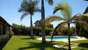 A well-maintained backyard with a swimming pool, palm trees, and a lawn. - Country house in a gated community. (Sorocaba)