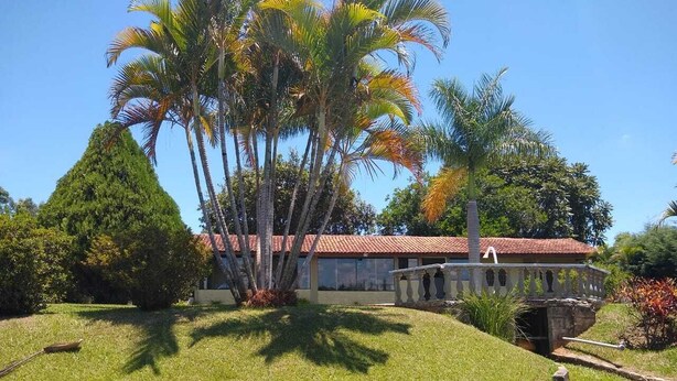A house with a red-tiled roof, surrounded by a well-maintained lawn and palm trees. - Country house in a gated community. (Sorocaba)