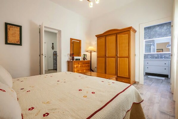 A bedroom with a bed, wooden wardrobe, dresser, and a bathroom with a vanity and mirror. - Villa del Manzano, Complete villa with pool just 15 minutes from Seville (Villanueva del Ariscal)