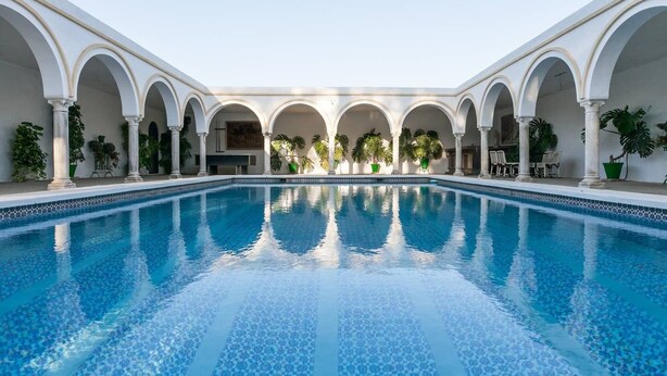 A swimming pool with a tiled pattern, surrounded by white columns and arches, with potted plants and outdoor seating. - Villa del Manzano, Complete villa with pool just 15 minutes from Seville (Villanueva del Ariscal)