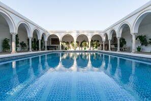 A swimming pool with a tiled pattern, surrounded by white columns and arches, with potted plants and outdoor seating. - Villa del Manzano, Complete villa with pool just 15 minutes from Seville (Villanueva del Ariscal)