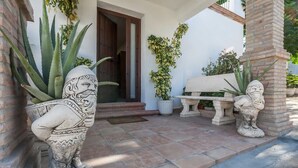 A patio area with a stone bench, a decorative planter with a carved figure, and a door leading to the interior. - Villa del Manzano, Complete villa with pool just 15 minutes from Seville (Villanueva del Ariscal)
