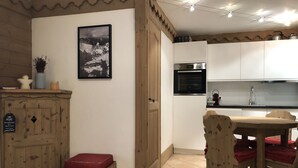 A compact kitchen with white cabinets, a built-in oven, and a dining area with wooden chairs and a red cushion. - Charming 3 rooms 3* residence Swimming pool, sauna, gym in Méribel Village (Méribel Village)