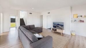 Ett modernt vardagsrum med en grå hörnsoffa, en platt-TV på ett träställ och en trappa som leder ut till ett utomhusområde.