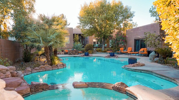 A swimming pool with a curved design, surrounded by rocks and plants, and adjacent to a building with outdoor seating.