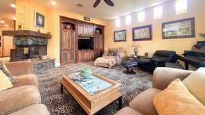 A living room with a stone fireplace, leather sofas, a coffee table with photos, a television, and framed artwork on the walls.