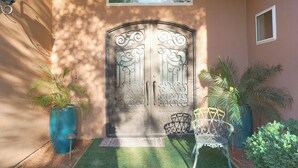 A wrought iron gate with intricate designs, flanked by potted plants and a bench.