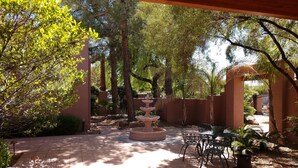 A covered patio area with a stone fountain, outdoor seating, and a view of the surrounding trees.