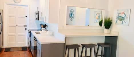 A modern kitchen with white cabinets, a built-in island with bar stools, a clock, and a potted plant.