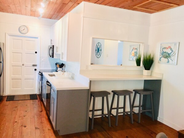 Een moderne keuken met witte kasten, een inbouw-kookeiland met barkrukken, een klok en een potplant.