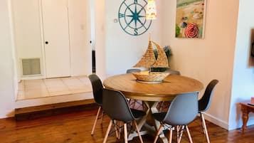 Un coin repas avec une table ronde en bois, quatre chaises, une pièce décorative en forme de bateau tressé, une boussole fixée au mur et un tableau sur le thème de la plage.
