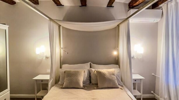 Quarto com uma cama grande, vigas de madeira, paredes brancas e mesas de cabeceira com luminárias.