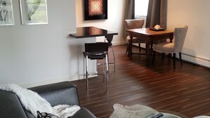 Ein modernes Wohnzimmer mit einem dunkelgrauen Ledersofa, einem flauschigen weißen Teppich und einem Essbereich mit einem Holztisch und Stühlen.