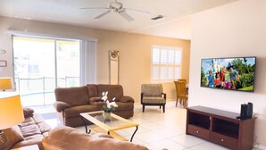 Una sala de estar con ventilador de techo, televisor, sofá, mesa de centro y comedor con una silla y mesa.