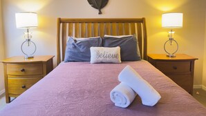 Una cama bien hecha con una colcha rosa, dos almohadas, una toalla enrollada y dos mesitas de noche con lámparas.