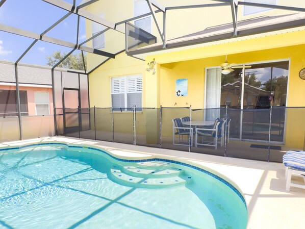 An indoor swimming pool with a glass enclosure, a yellow wall, and a table with chairs.