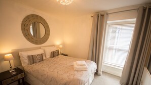 A neatly made bed with a patterned bedspread, a round mirror on the wall, and a bedside table with a lamp. - Ideal location for enjoying all of Tenby's attractions (Tenby)