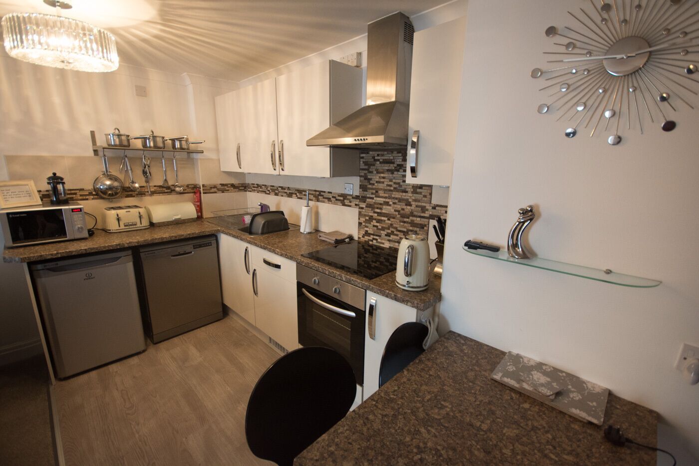 A modern kitchen with granite countertops, stainless steel appliances, and a unique wall clock.