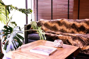 Une pièce avec un canapé marron à l’aspect duveteux, une table basse en bois sur laquelle se trouvent un livre et une sphère décorative, ainsi qu’une grande plante verte.