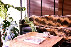 A room with a brown furry sofa, a wooden coffee table with a book and a decorative sphere, and a large green plant.