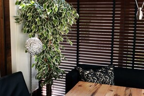 Een kamer met een houten tafel, zwart-wit gestreepte kussens, een hangplant en een decoratieve lamp.