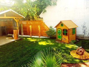 A backyard with a wooden playhouse, a small shed, a tree, and a lawn.