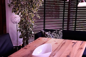 Une table en bois, sur laquelle se trouve un bol blanc, un luminaire sphérique suspendu et une plante aux feuilles panachées.