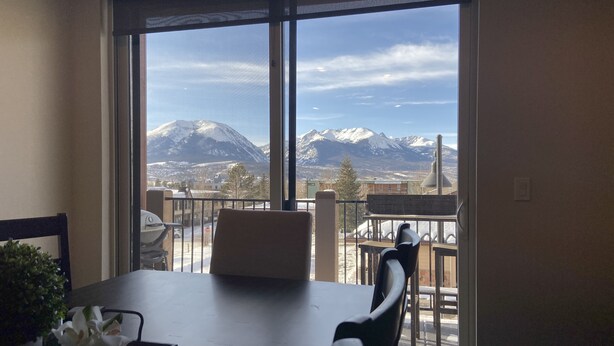 A dining area with a table and chairs, a view of snow-capped mountains, and a balcony with a railing. - Spacious New Condo - Beautiful Views in the Heart of  Dillon. License# 651848101 (Dillon)