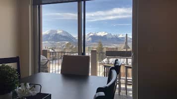 A dining area with a table and chairs, a view of snow-capped mountains, and a balcony with a railing.