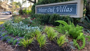 A sign for Water Oak Villas with a landscaped garden featuring various plants and trees.