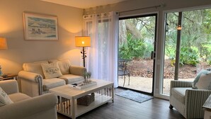 A living room with a sofa, armchairs, a coffee table, and a view of the outdoors through a glass door.