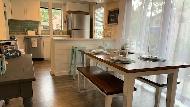A modern kitchen with a wooden dining table set for four, a refrigerator, and a window with blinds.