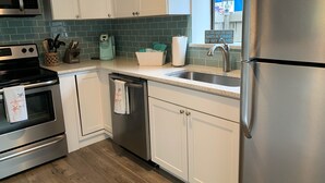 A modern kitchen with stainless steel appliances, white cabinets, a wooden floor, and a view of the outside through a window.