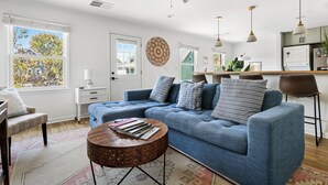 Un salon moderne avec un canapé bleu, une table basse et un coin repas, la cuisine étant visible au fond.