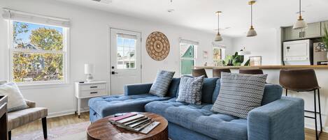 A modern living room with a blue sofa, a coffee table, and a dining area with a kitchen in the background.